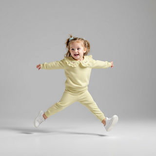 Child in a light yellow outfit jumping against a gray background